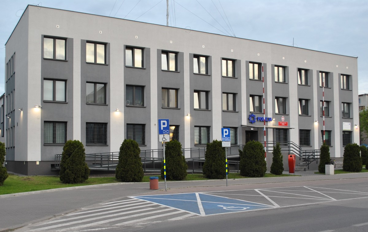 budynek Komendy Powiatowej Policji w Łukowie, przed nim parking samochodowy z wyznaczonym miejscem dla osób z niepełnosprawnościami