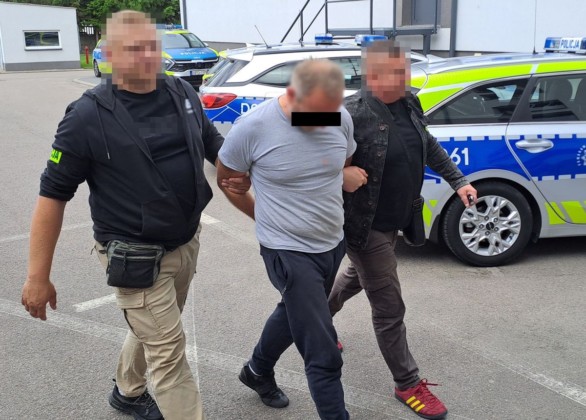 nieumundurowani policjanci prowadzą podejrzanego, w tle radiowozy i ściana budynku