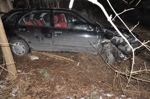 Stojący w zagajniku uszkodzony samochód marki Nissan.