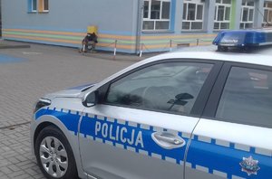 Radiowóz i policjant sprawdzający teren przy budynku.