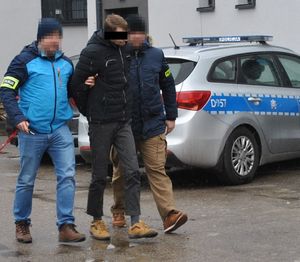 policjanci doprowadzają zatrzymanego, w tle oznakowany radiowóz