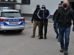 nieumundurowani policjanci prowadza podejrzanego, w tle policyjny radiowóz