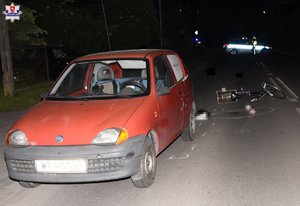 Fiat Seicento i uszkodzony rower na miejscu zdarzenia drogowego, w tle radiowóz policyjny