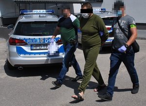 nieumundurowani policjanci prowadzą jednego z podejrzanych, w tle radiowóz policyjny