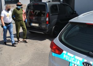 nieumundurowani policjanci prowadzą jednego z podejrzanych, w tle radiowóz policyjny