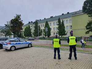 Na zdjęciu widoczna szkoła. W pierwszym planie radiowóz oraz dwóch policjantów.