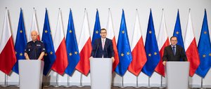 Na zdjęciu od lewej:  gen. insp. Jarosław Szymczyk – Komendant Główny Policji, premier Mateusz Morawiecki i Minister Spraw Wewnętrznych i Administracji Mariusz Kamiński. W tle flagi Polski i Unii Europejskiej