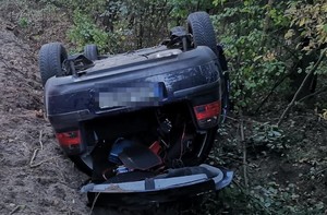 tył leżącego na dachu samochodu marki Volkswagen, w tle gałęzie drzew pobliskiego lasu