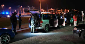 stojące na parkingu samochody, policjanci i postronne osoby, w tle radiowóz i stacja kolejowa