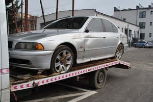 samochód marki BMW na lawecie, w tle budynek i radiowozy