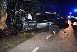 stojący przy drzewie uszkodzony samochód marki Audi, w tle radiowóz