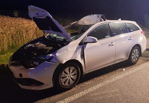 uszkodzony samochód marki Toyota, w tle rosnące na polu zboże i strażak