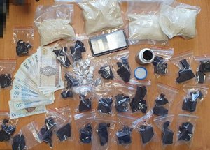 leżące na stole foliowe woreczki z brązowo-brunatną i sproszkowaną substancją, banknoty i elektroniczna waga