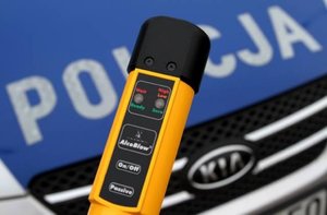 AlcoBlow, w tle pokrywa silnika radiowozu z napisem POLICJA