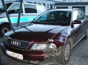 samochód marki Audi z uszkodzonymi elementami karoserii, w tle radiowóz