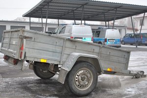 przyczepka samochodowa, w tle oznakowane radiowozy i granatowy pojazd typu bus