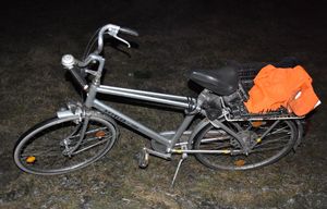 stojący na trawiastym podłożu rower, ze znajdująca się w koszyku kamizelką odblaskową