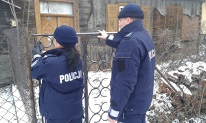 policjanci wchodzą na teren ogrodzonej posesji, w tle drewniany budynek