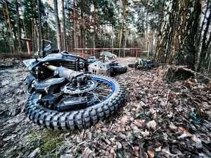 leżący na leśnej drodze uszkodzony motocykl marki Yamaha, w tle metalowy szlaban i policyjny radiowóz