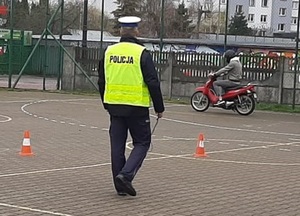 idący po placu manewrowym policjant, obok jadący motorowerem uczestnik konkursu