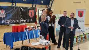 policjanci, Burmistrz, maskotka Komisarz Miś, w tle baner konkursu