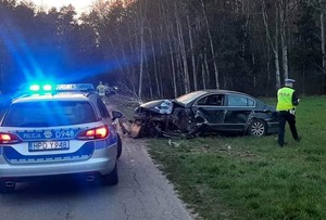 stojący na drodze radiowóz, stojący na drodze uszkodzony Volkswagen obok policjant