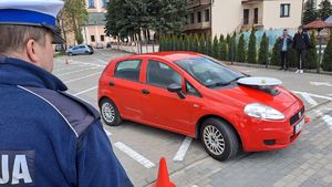 czerwony samochód osobowy z talerzem Stewarta, obok policjant