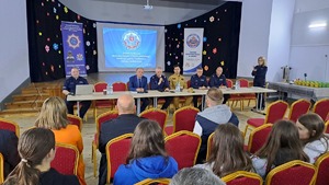 osoby siedzące na krzesłach, w tle policjanci i ekran