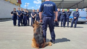 policjant i pies, w tle uczniowie i radiowóz