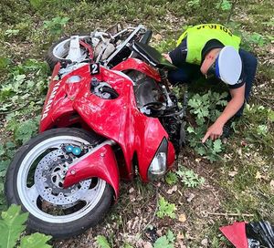 leżący na trawiastym podłożu motocykl Yamaha, obok policjant