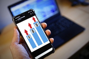 dłoń ze smartfonem, w tle ekran laptopa