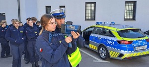uczennica klasy policyjne i policjant z miernikiem prędkości, w tle uczniowie i radiowóz