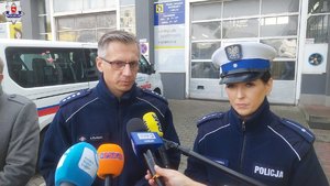 mikrofony i policjanci, w tle ściana budynku i samochód