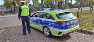 policjant drogówki i radiowóz, w tle teren cmentarza