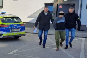 podejrzany prowadzony przez nieumundurowanych policjantów, w tle radiowóz