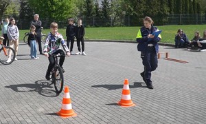 uczeń jadący rowerem na torze przeszkód, w tle policjant
