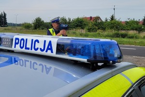 policjant z radarowym miernikiem prędkości, dach radiowozu z napisem policja