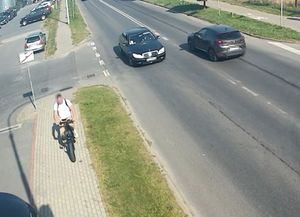 mężczyzna jadący rowerem po chodniku, w tle samochody jadące po jezdni