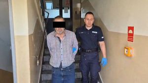 Policjant prowadzi zatrzymanego mężczyznę.