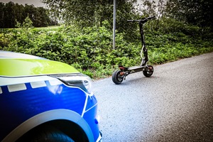 stojąca na jezdni elektryczna hulajnoga, obok radiowóz