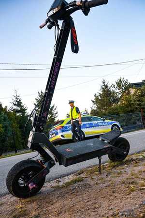 stojąca na drodze hulajnoga, w tle policjant i radiowóz