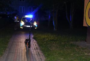 stojąca na osiedlowej alejce hulajnoga, w tle radiowóz