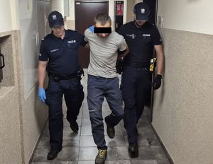 policjanci prowadzą po korytarzu zatrzymanego mężczyznę