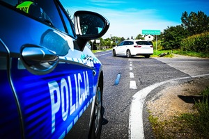 miejsce wypadku drogowego, radiowóz, samochód osobowy i rower leżący na poboczu