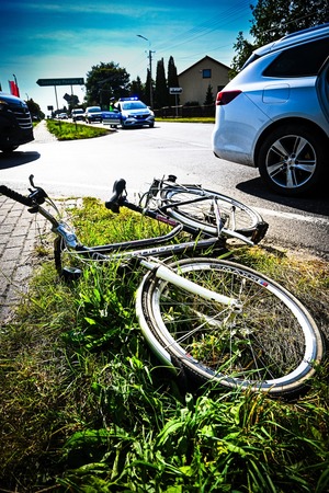uszkodzony rower leżący na poboczu, obok droga i samochody
