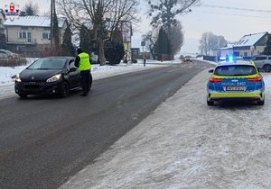 policjant sprawdzający stan trzeźwości kierującego samochodem osobowym, obok radiowóz na zaśnieżonej drodze
