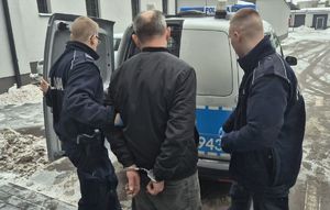policjanci umieszczają w radiowozie zatrzymanego mężczyznę, który ma kajdanki nałożone na ręce trzymane z tyłu