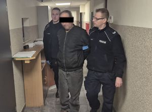 policjanci prowadzą po korytarzu zatrzymanego mężczyznę