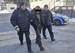 umundurowani policjanci prowadzą zatrzymanego, w tle radiowóz