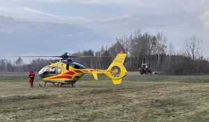 śmigłowiec LPR na polu w tle drzewa i ciągnik roliczy